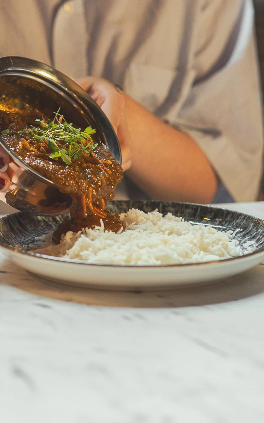 Curry poured from a copper pot over steamed rice