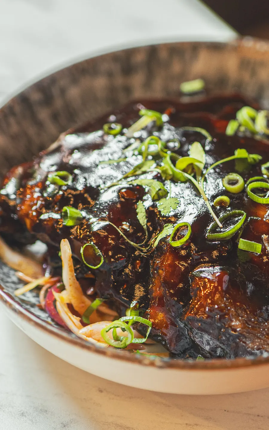 Sticky ribs in a dark glaze, scattered with spring onion