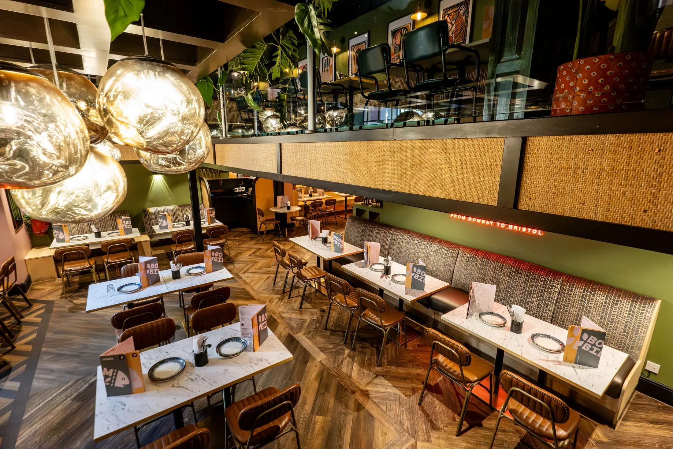 Bombil's main dining room under clusters of smoked-glass globe lamps, with rattan panels and long booths